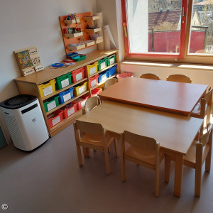 Foto: Gruppenraum mit Tischen und Kommode mit bunten Schubladen